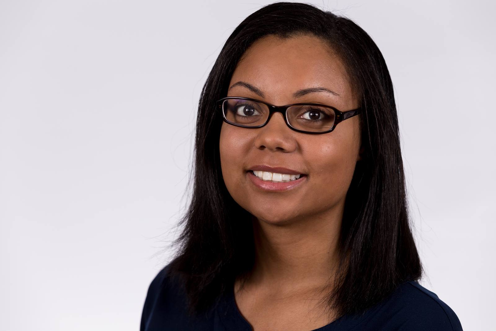 Head-and-shoulders portrait of a woman with dark hair and glasses, smiling against a plain white background.