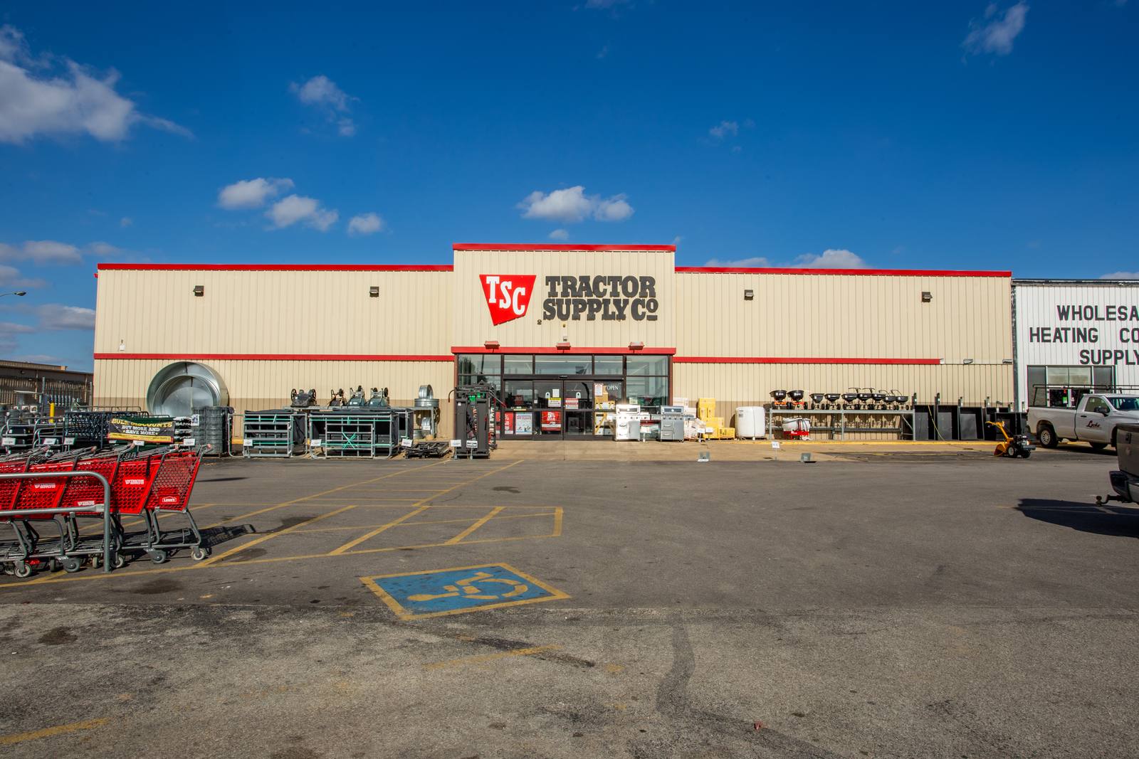 A wide exterior shot shows a Tractor Supply Co. store with red-trimmed facade, parking lot, shopping carts, and merchandise displays under a blue sky.